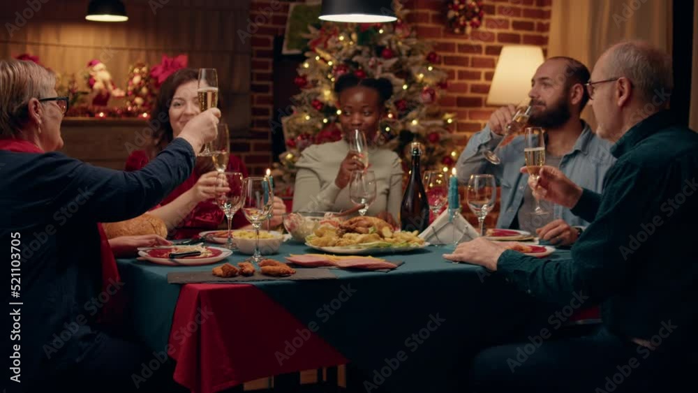 Festive happy woman toasting with family members while enjoying home cooked Christmas dinner at home. Joyful multiethnic people celebrating traditional winter holiday while drinking sparkling wine. Festive happy woman toasting with family members while enjoying home cooked Christmas dinner at home. Joyful multiethnic people celebrating traditional winter holiday while drinking sparkling wine.