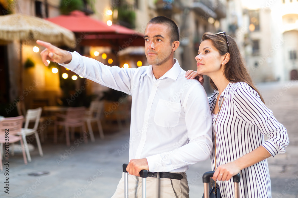 Fototapeta premium Young positive tourist couple walking around foreign city on summer day, pointing at sights
