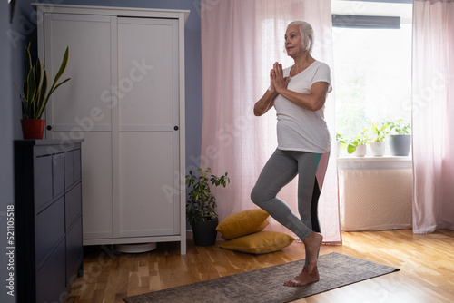 Positive mature lady standing in tree pose, keeping balanced exercising