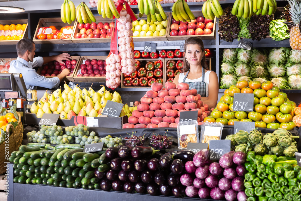 Young female vendor offers fresh ripe fruits and vegetables at the grocery store.