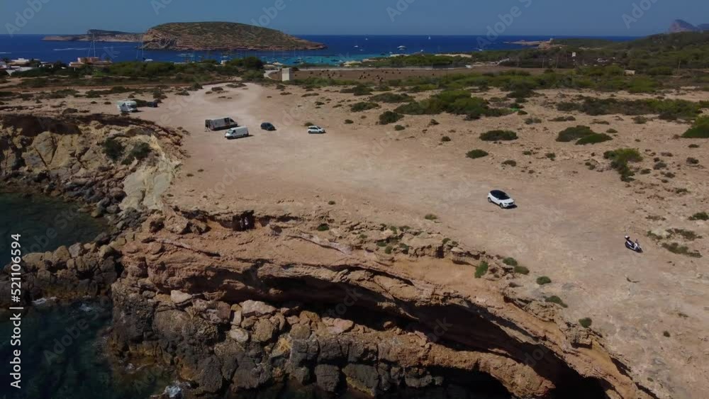 Cars and scooter parking on the cliff edge.
Great aerial view flight panorama curved flight drone footage
of cliff beach Sa Figuera borda Ibiza summer 2022. 4k Cinematic from above by Philipp Marnitz