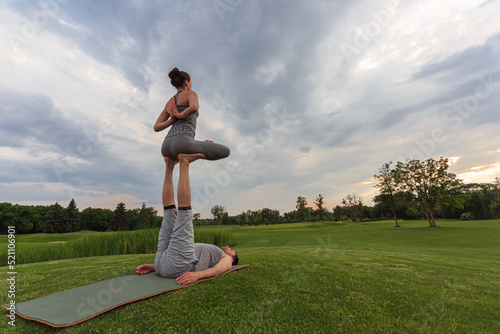 Man lying on grass and balancing woman in his feet. Young couple doing acro yoga in park