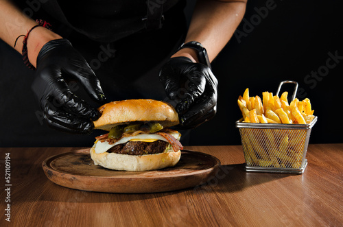 The photograph shows the preparation of a hamburger accompanied by French fries.