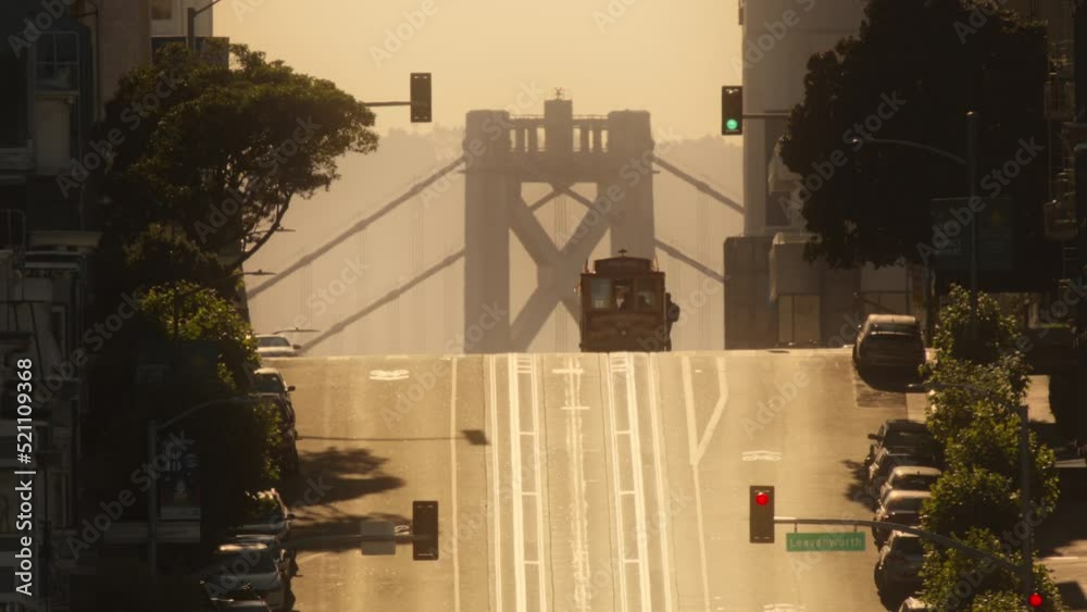 Scenic time lapse with old historic cable car tram riding up the hill in San Francisco. Silhouette of tourist landmark attraction tram at Bay Bridge background, early weekend morning golden sunrise