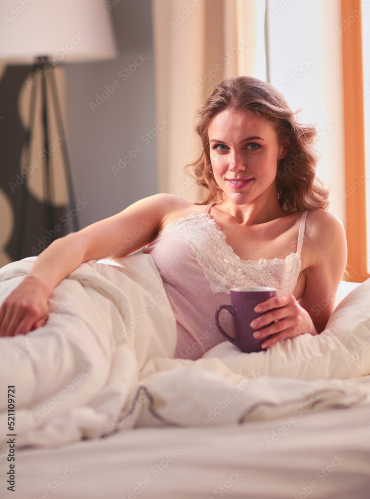 Young woman drinking cup of coffee or tea while lying in bed.