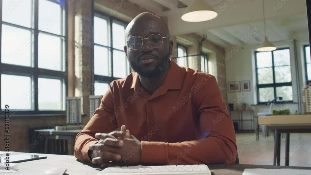 African American man sitting at desk in architectural office, waving and talking on camera while filming business vlog African American man sitting at desk in architectural office, waving and talking on camera while filming business vlog