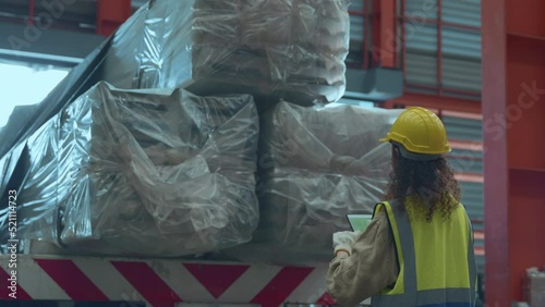 Industrial woman curly hair engineer wear safety uniform with hardhat checking metal sheet on cargo truck before shipment to customer in warehouse store factory workshop, logistics and transportation