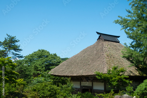 夏の青空と緑の中のお寺の茅葺き屋根