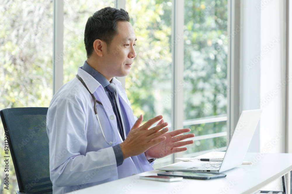 Asian senior doctor sitting in medical office while video call meeting using laptop computer. Asian senior doctor sitting in medical office while video call meeting using laptop computer.