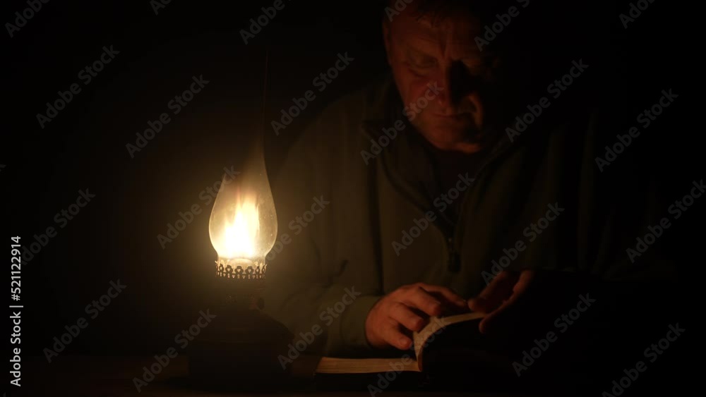 Man reads a book by the light of a kerosene lamp at night time, close up