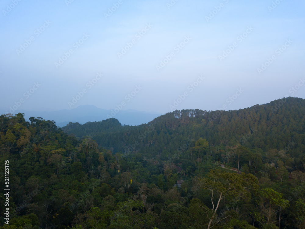 A panoramic view of the foggy Mountains with dense of forest. Blue sky with clouds over layers of green hills and mountains. Copy space.  Menoreh Hill, Central Java, Indonesia