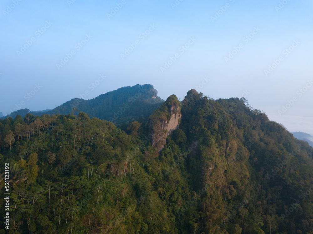 A panoramic view of the foggy Mountains with dense of forest. Blue sky with clouds over layers of green hills and mountains. Copy space.  Menoreh Hill, Central Java, Indonesia