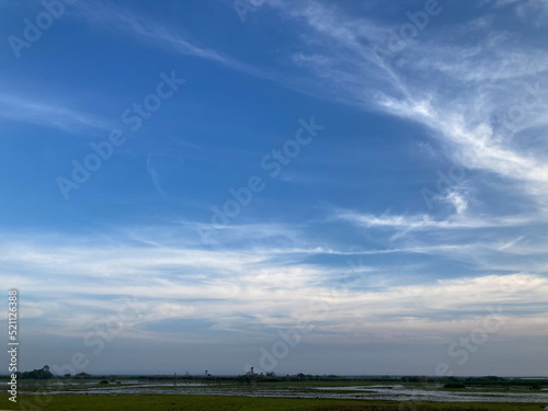 view of green fields and river with wide clear bright blue sky and white clouds of countryside
