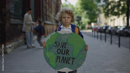 Little boy standing outdoor against enviroment pollution loooking at camera. Little eco activist demostration on the street. Eco concept photo