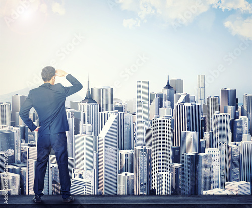 Business man looking at cgi, digital and artificial buildings while standing alone at work from behind. Back of one male corporate professional, manager or employee analysing and examining the view