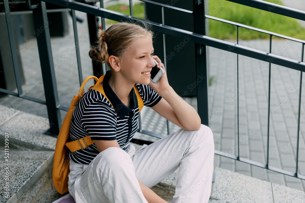 Fototapeta premium A beautiful girl is sitting on the stairs at school in between classes and talking on the phone