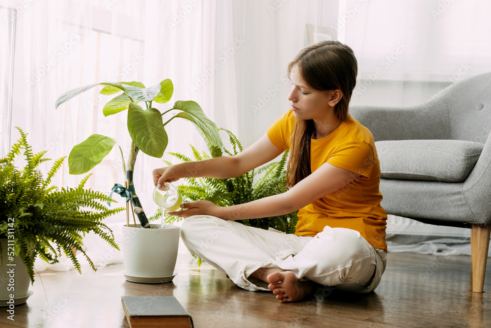 A young happy girl is watering potted plants with water in her small home garden. She is sitting cross-legged on the floor A young happy girl is watering potted plants with water in her small home garden. She is sitting cross-legged on the floor