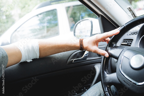 To drive a car with an injured hand, a bandaged elbow arm hurts, a road injury, a person sits inside the car, dislocated elbow.