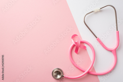 Breast cancer awareness concept. Top view photo of pink satin ribbon and stethoscope on bicolor pastel pink and white background with empty space