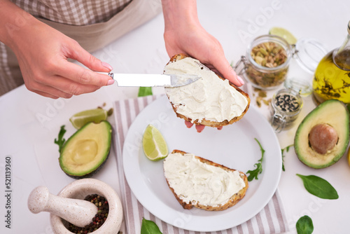 Avocado and cream cheese toasts preparation - Woman smearing cheese on a grilled or toasted bread