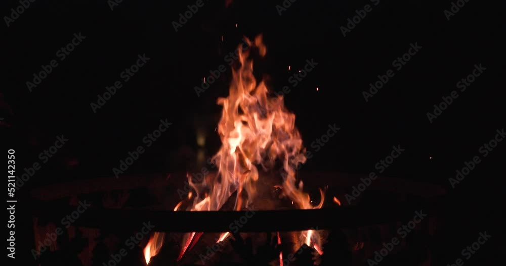 side angle of man poking fire pit with log.