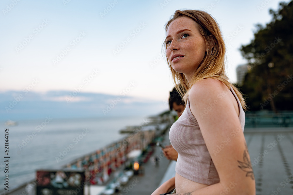 Beautiful young woman standing and looking at the sea and sky