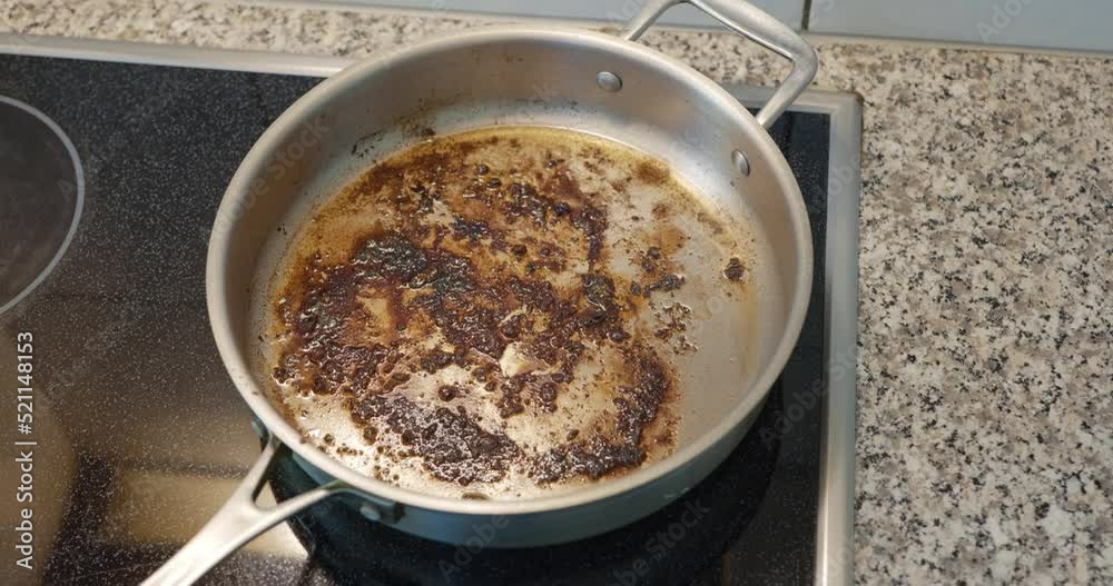 Dirty oily burnt metal frying pan sizzling on an electric stove. Sticky