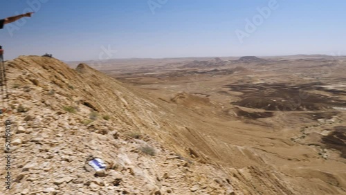 Side view of Young Man Trekker on the Top of Sandstone Mountain Ridge Pointing with Hand on Endless Negev desert while Travel in Ramon Crater Trail, Israel photo