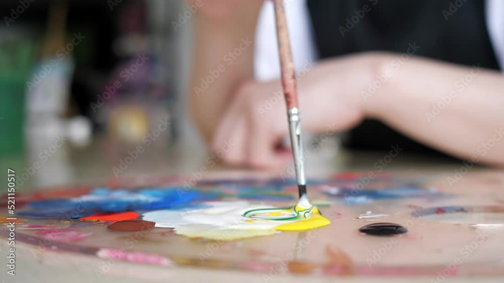 Person mixes bright gouache paint colours on palette using paintbrush. Skilled artist mixes paints to get new colours for painting on canvas closeup, side view Person mixes bright gouache paint colours on palette using paintbrush. Skilled artist mixes paints to get new colours for painting on canvas closeup, side view