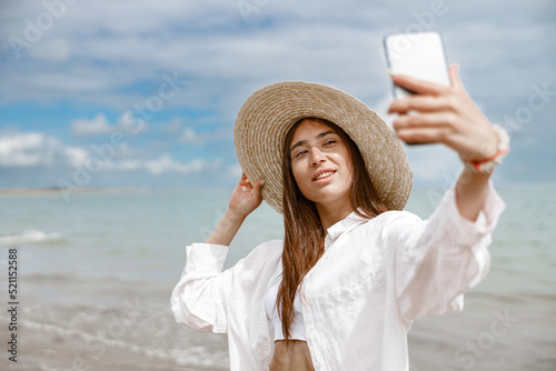 Beautiful woman in hat standing on beach near sea and making selphie photo