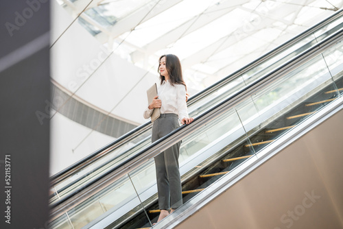 Young business woman holding a briefcase in hand riding an escalator