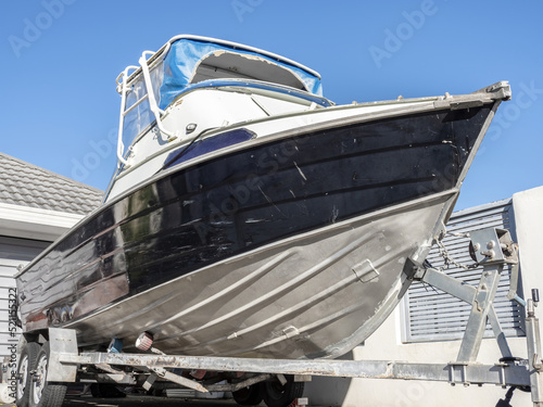Small aluminum motorboat on trailer parked in driveway.