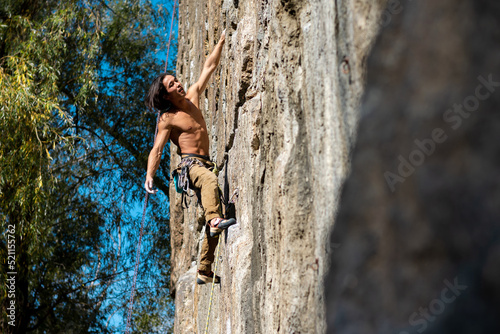 Athletic man in a harness climbs a rock