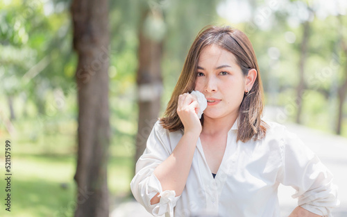 Young pretty girl drying sweat using tissue on a warm summer day in a park, Woman in the park having sunstroke in summer hot weather
