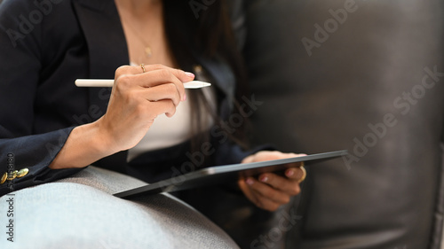 Cropped view of female entrepreneur sitting on couch in her personal office and using digital tablet