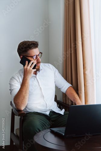 Obraz na płótnie Male businessman in a white shirt working at a laptop in the office, during a conversation, online meeting, remote work. w salonie
