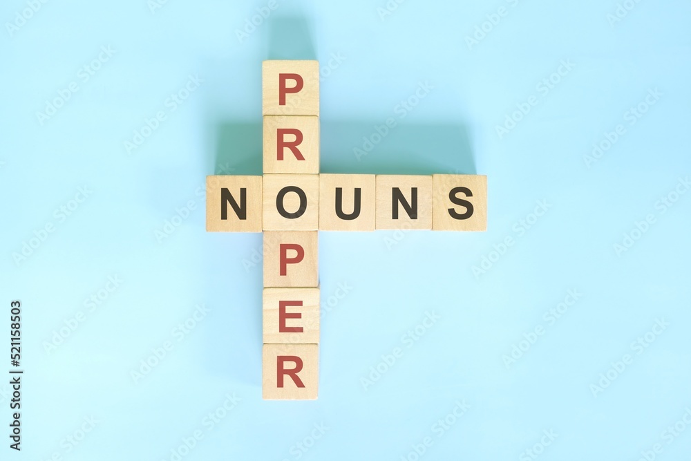 Proper nouns concept in English grammar education. Wooden block crossword puzzle flat lay in blue background. Proper nouns concept in English grammar education. Wooden block crossword puzzle flat lay in blue background.