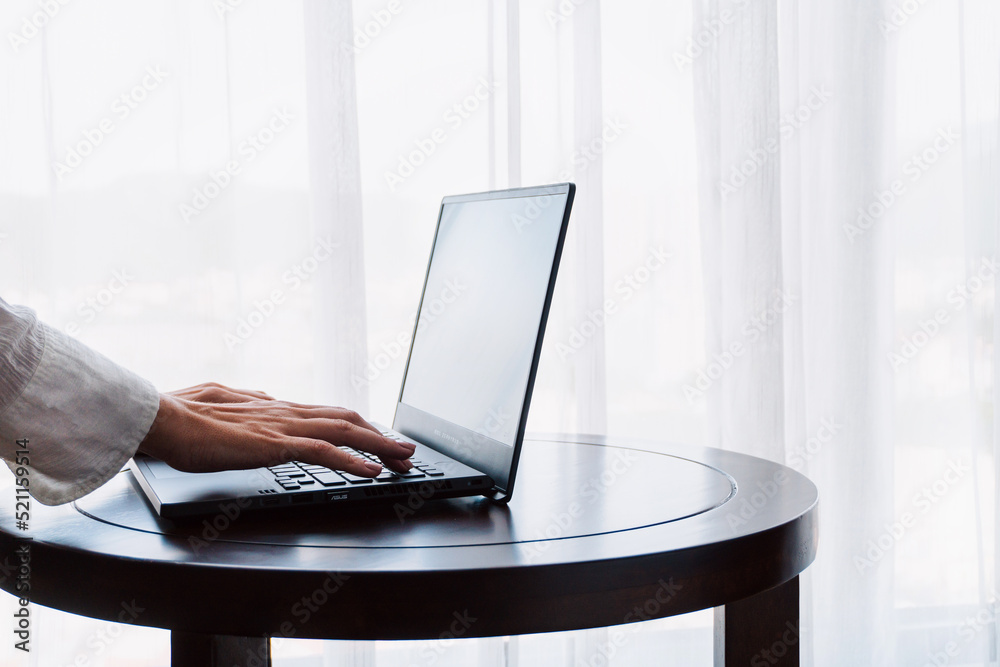 Person working at a laptop, close-up of hands and computer screen, remote work on a light background.
