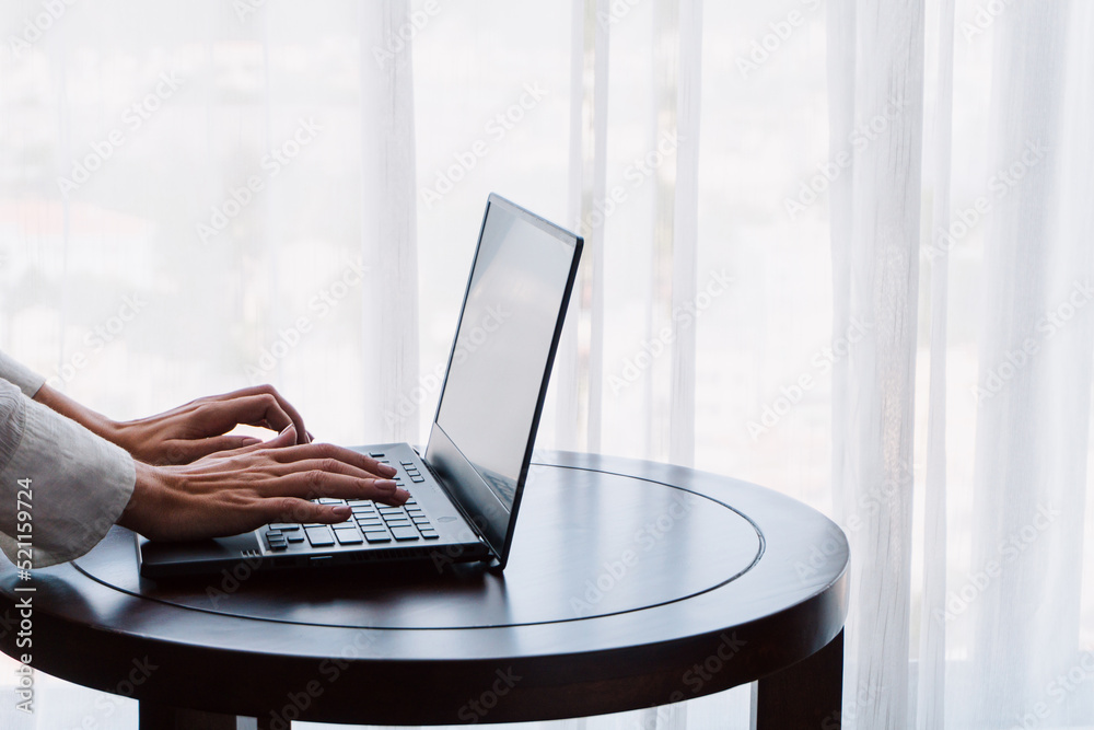 Person working at a laptop, close-up of hands and computer screen, remote work on a light background.