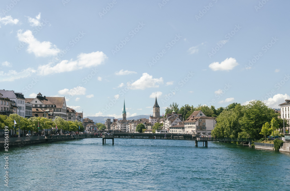 Panorama of Zürich, Switzerland and one of its many bridges over the main city river, with typical old historic buildings all around on a blue sky sunny summer day