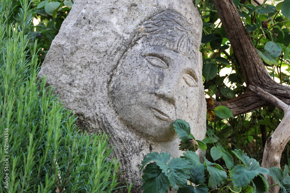 verwitterte Steinskulptur im Garten, Buddah vor einem Rosmarin und einer Erdbeerpflanze
