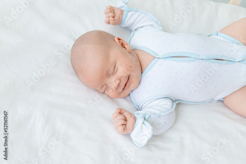 smiling or laughing in a dream, a newborn baby boy sleeps for seven days in a cot at home on a cotton bed, close-up