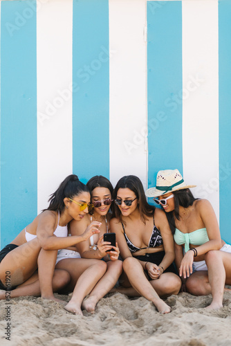 Four young women in bikinis using smart phones leaning against the beach wall