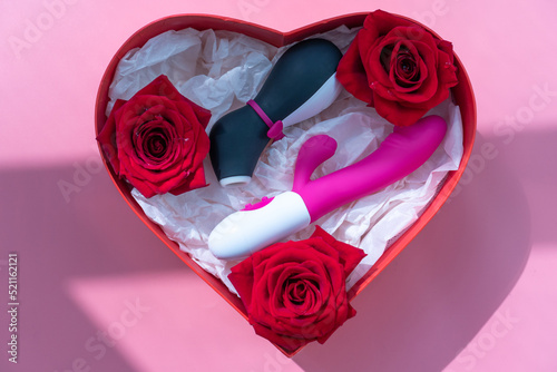 Satisfyer pro penguin, the most famous dildo for women and a pink vibrator in a heart shaped gift box on a pink background. Shadow from the window. Gift concept for adults from online sex shop.  photo