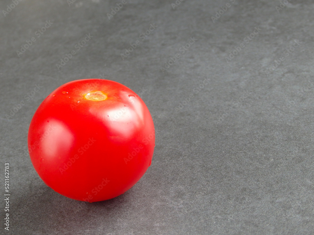 Fresh organic tomato on grey background. One ripe red tomato on a dark background close-up Fresh organic tomato on grey background. One ripe red tomato on a dark background close-up