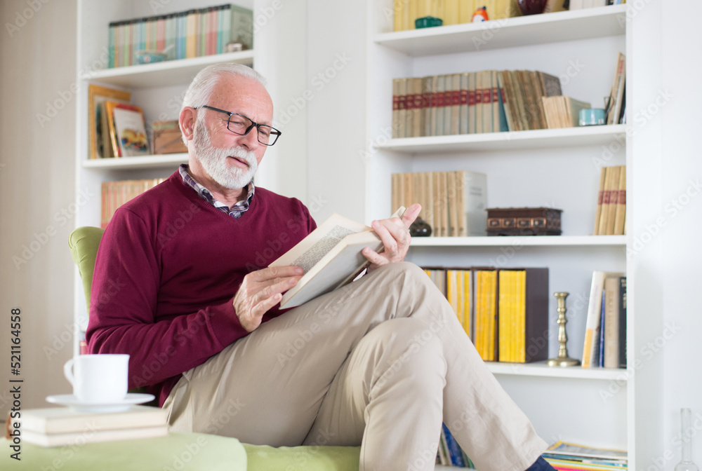 Senior man reading book from his home library and drinking coffee in the morning Senior man reading book from his home library and drinking coffee in the morning