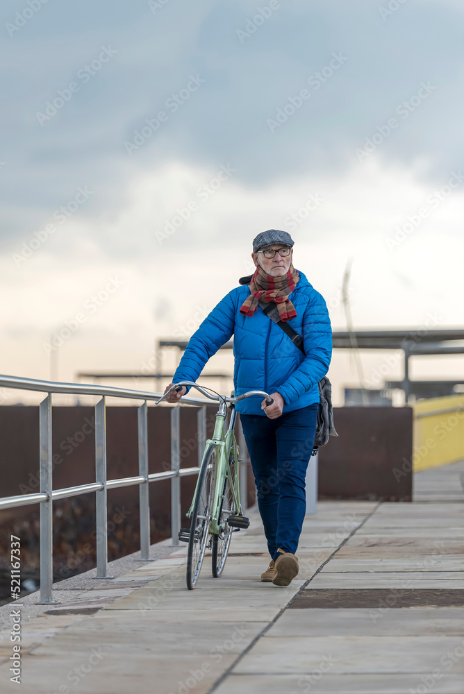 Handsome senior man walking with bike on seafront