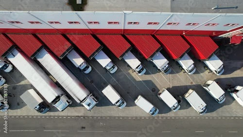Aerial top view of an industrial warehouse loading dock, where many delivery vans and trucks load goods. The logistics center and vehicles waiting to be loaded or unloaded.