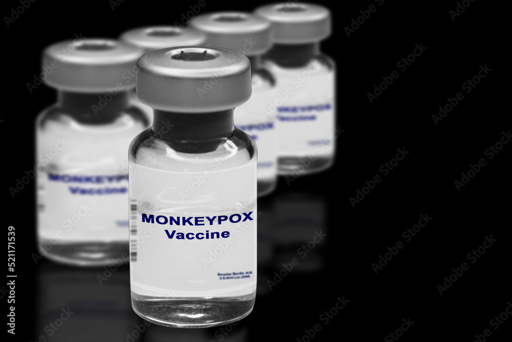 Monkeypox vaccine close-up on a black mirror background. In the background are blurred vaccine vials. Monkeypox vaccine close-up on a black mirror background. In the background are blurred vaccine vials.