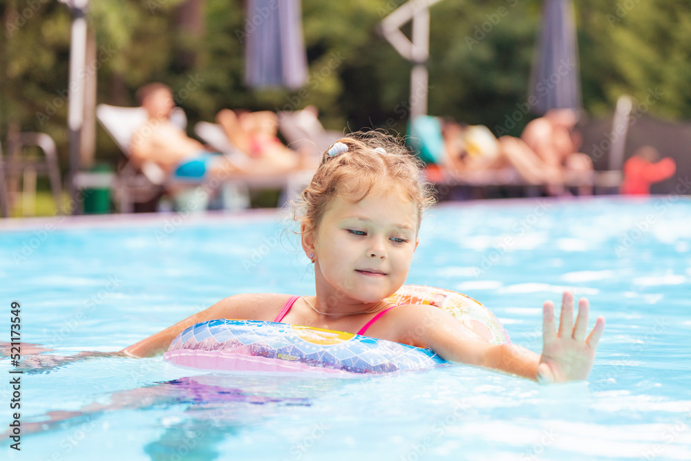 Beautiful cute little girl swims in the outdoor pool with an inflatable ring